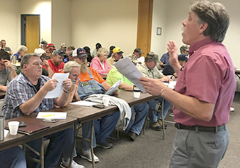 A department employee standing at the front  of a conference room conducting training for a large room of trainees