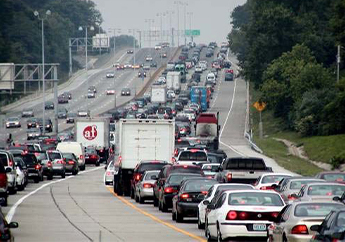 Two lines of trucks and cars merging into heavy traffic on an six lane highway.