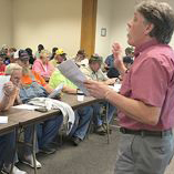 A department employee standing at the front  of a conference room conducting training for a large room of trainees