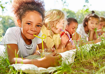 Children laying on their stomachs on a blanket in the grass enjoying something to drink