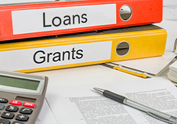 Two 3-ring binders on a table, an orange binder marked "loans" and a yellow marked "Grants", with a calculator, pen and paper copy of terms in front of the binders 