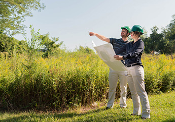 Two MoDNR staff wearing hardhats in a field, identifying locations with a map