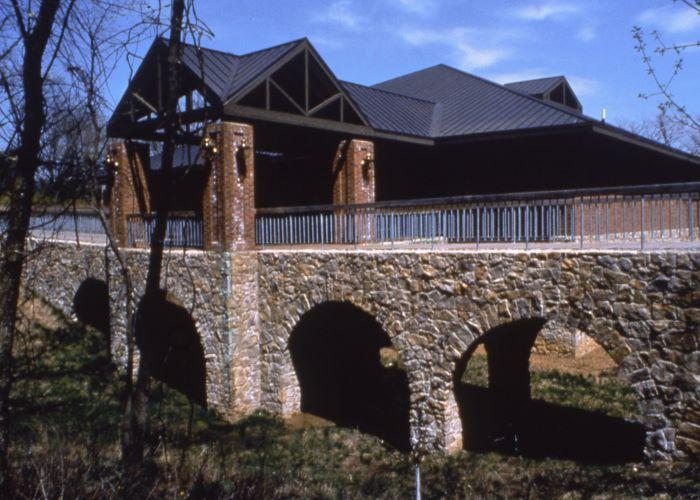 Four stone arches with bridge and handrail on top going to a metal-roofed building