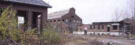 Brownfields property with several dilapidated buildings and weed-covered open spaces 