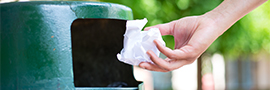A hand throwing away paper in a green trashcan